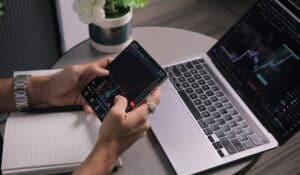 Man analyzing stock trends with laptop and mobile trading app at a modern workspace. — Photo by Kaushal Moradiya on Pexels