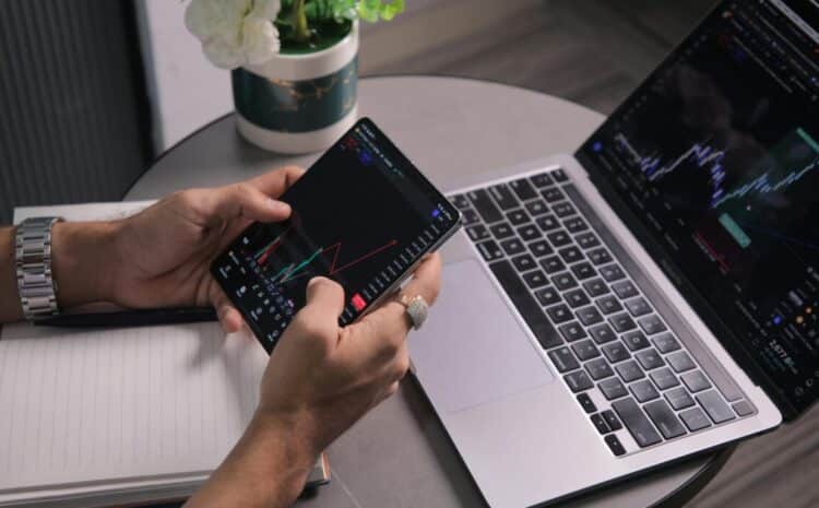 Man analyzing stock trends with laptop and mobile trading app at a modern workspace. — Photo by Kaushal Moradiya on Pexels